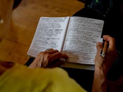 the hands of an elder in the gathering hold a notebook on their lap with two pages visibly packed full of notes.