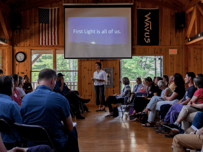 Kate Stookey, director of Maine Coast Heritage Trust, speaks to the full group about her belief in First Light's work with a slide behind her that says "First Light is all of us."