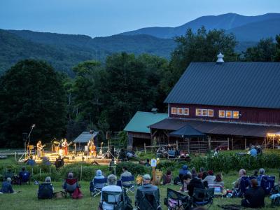 People sit on a hillside overlooking a valley, listening to a live concert by Lula Wiles at Knoll Farm