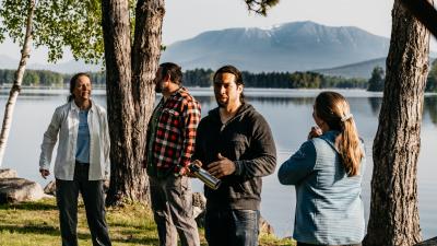 Native and nonnative people talking in front of lake and mountain.