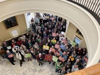 A large group of people hold up signs at the Maine State House during Lobby Day