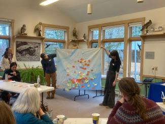 Two people hold up a large map of Maine, filled with colorful notes
