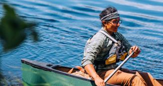 Damon Galipeau, a cohort 2 grantee, pictured on the water paddling in a green canoe and life jacket.