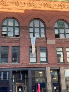 a colorful banner that says "COURAGE"  hangs from the large arched windows of the Bangor Arts Exchange, a beautiful old brick building in downtown Bangor, during the 2022 First Light Summit.