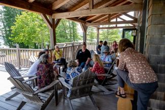 A group of non-native conservation leaders sit together on a shaded deck in a circle of adirondack chairs, discussing and sharing ideas.