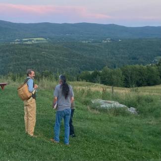 two men converse with field and mountains in background