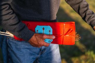 A person holds an intricately beaded red and blue pouch, containing eagle feathers