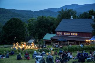 People sit on a hillside overlooking a valley, listening to a live concert by Lula Wiles at Knoll Farm
