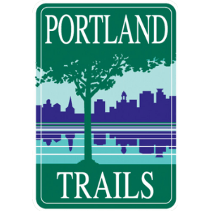A leafy tree on a grassy lawn in forest green on which the words, "Portland Trails," in white frame the rest of the image. In the background, an indigo blue Portland City skyline against a light blue sky is reflected in a calm turquoise bay.