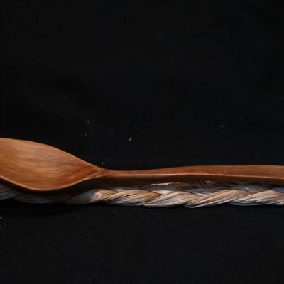 a wooden spoon, harvested and carved in a northern European linage, rests upon a braid of sweetgrass which was harvested and braided in the Wabanaki tradition.